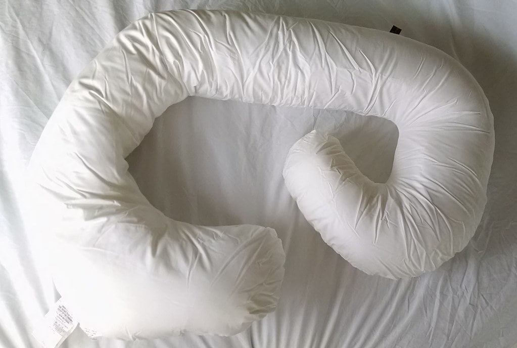 A white full body pregnancy pillow on the bed